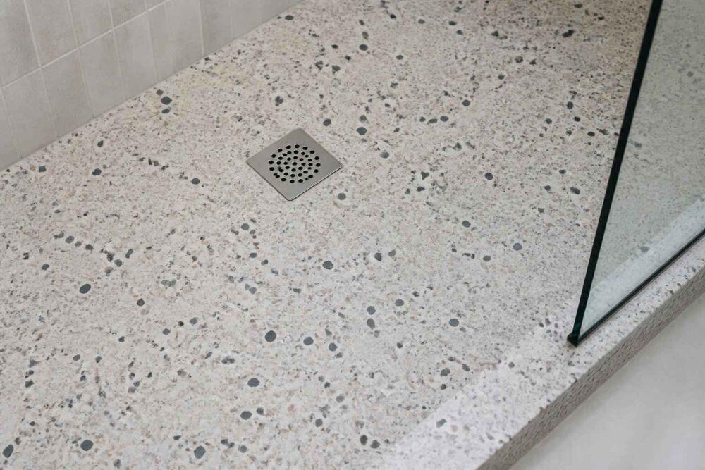 Terrazzo w brodziku prysznicowym z kwadratowym odpływem i szklaną kabiną