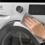 Dłoń przeciera ściereczką panel pralki Electrolux ładowanej od frontu