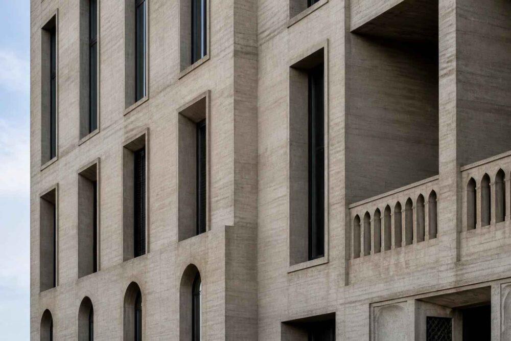Jasna betonowa fasada budynku z wąskimi oknami i arkadowymi detalami balustrady
