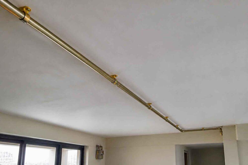 Miedziane rury instalacji poprowadzone pod sufitem w pomieszczeniu z oknami